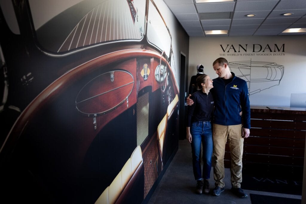 A man and woman embrace while standing in a lobby with large images displayed on the walls. 