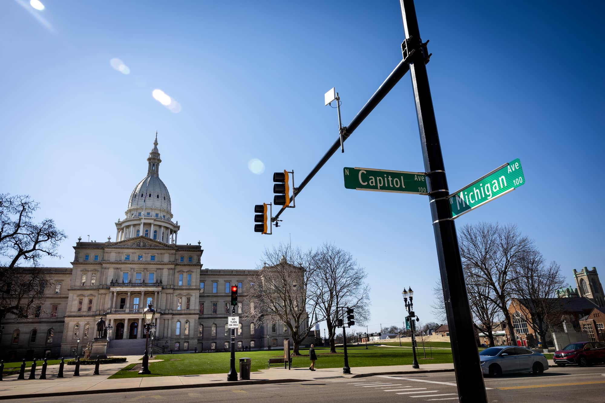 A view of the Michigan State Capitol building and surrounding city in Lansing, including a street intersection sign of Capitol and Michigan Aves on a clear day.