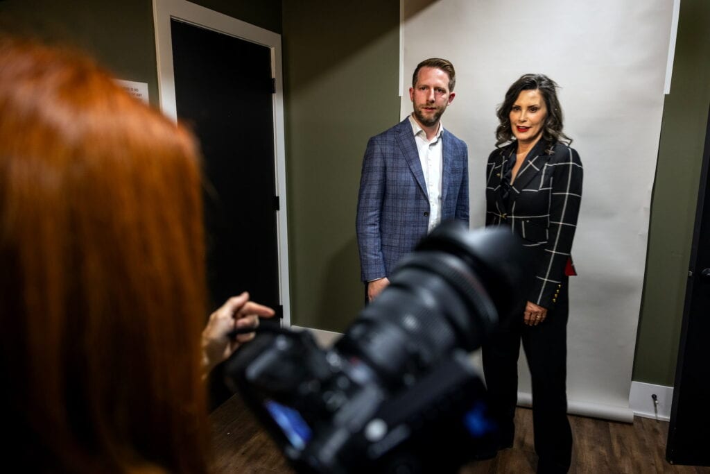 A photographer takes a portrait of a man and woman posing in front of a white backdrop.