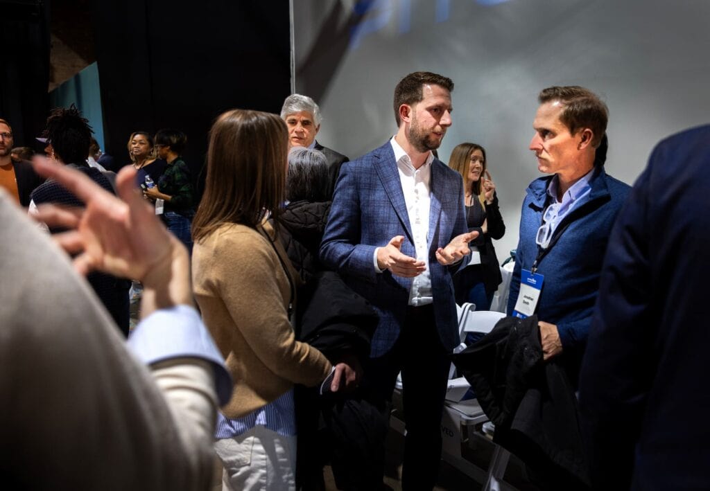 Several attendees in business attire talk in small groups during a networking session.