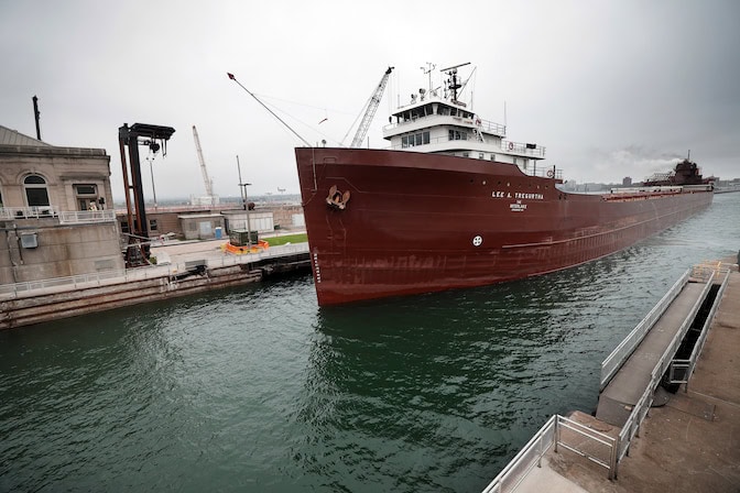 A lake freighter with a red hull enters a channel.