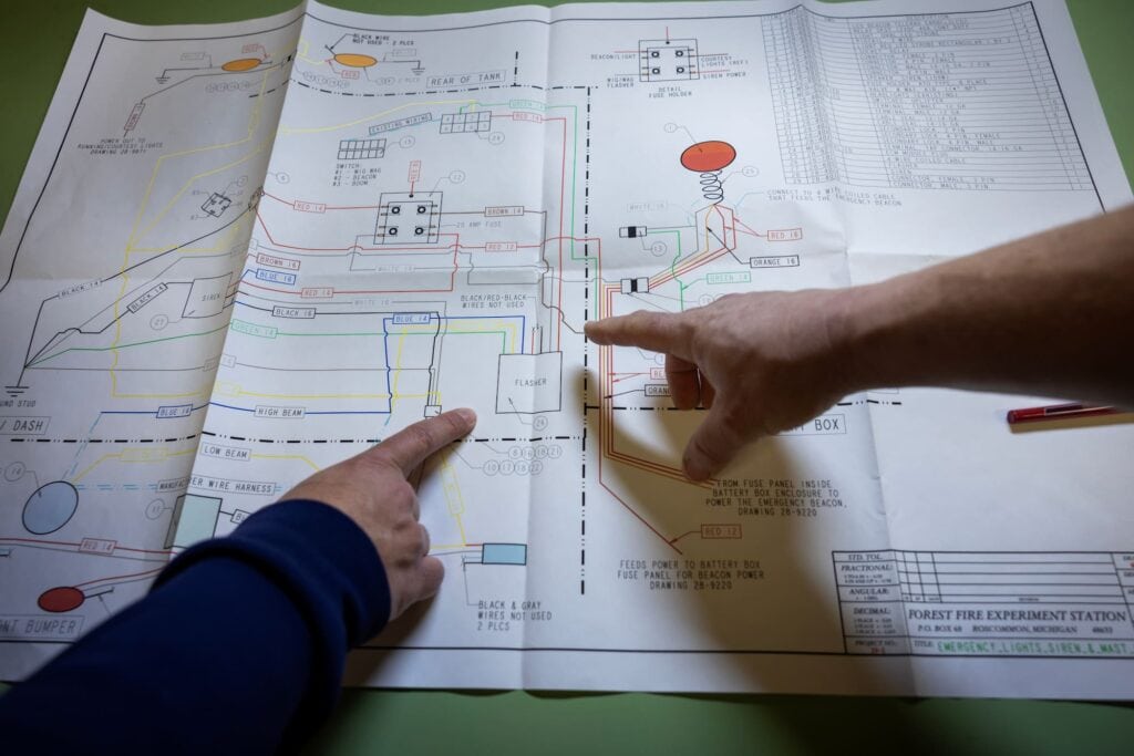 A close-up of hands pointing to specific details on a large set of technical diagrams.
