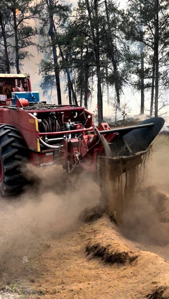 A specialized forestry machine creates a firebreak by churning soil and clearing vegetation.