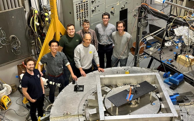 A photo of seven members of the research team standing in front of the MAIZE pulsed power facility in UM’s Plasma, Pulsed Power, and Microwave Laboratory.