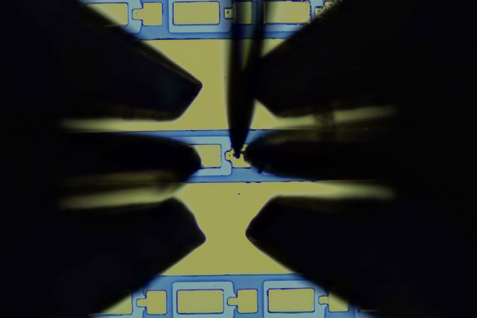 The metal-ferroelectric-metal capacitor structure is shown in gray while the probes appear as shadows, the right and left probes like miniature three-prong sporks and the rear probe coming from the top like the eye side of a needle.