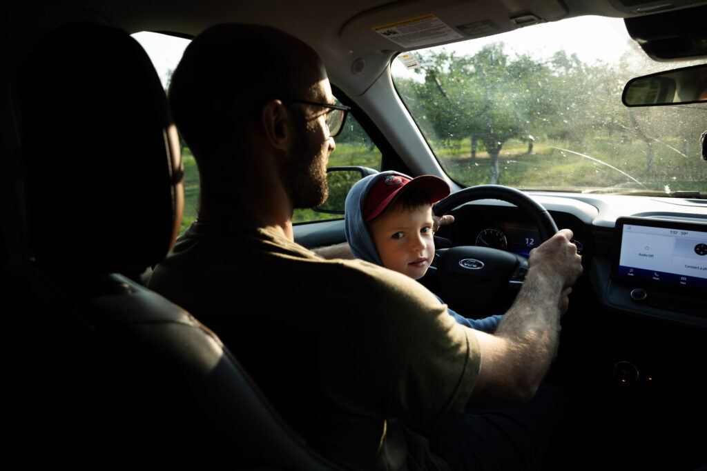 Chris Lyon drives through the orchard with his young son riding beside him in a truck.