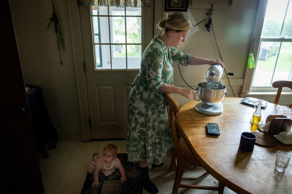 : A child sits on the floor as Julianne Lyon prepares food in the kitchen.