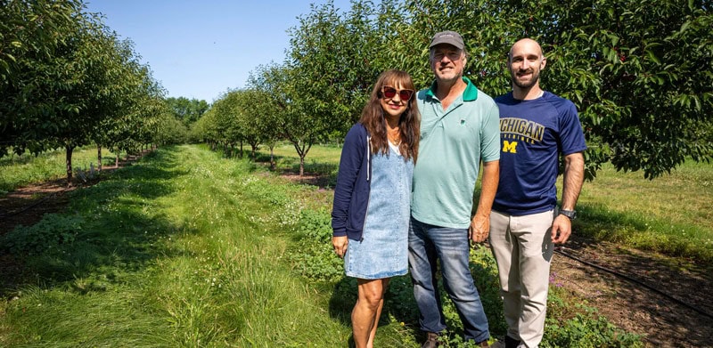 John, Gloria and Chris Lyon pose in front of a row of cherry trees on their farm.