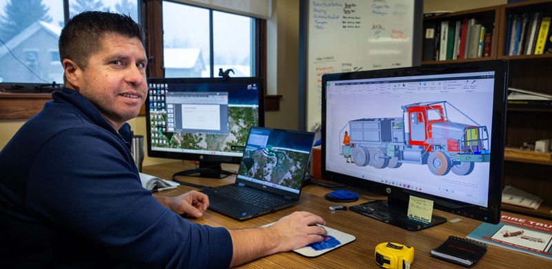 Dave Stockoski sits at a desk with a computer monitor displaying a 3-D rendering of a fire truck.