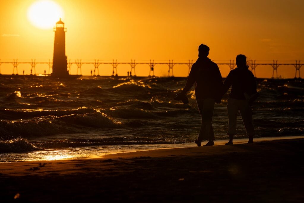 Waves crash against the Grand Haven Lighthouse and people walk on the beach during a colorful evening on Lake Michigan.