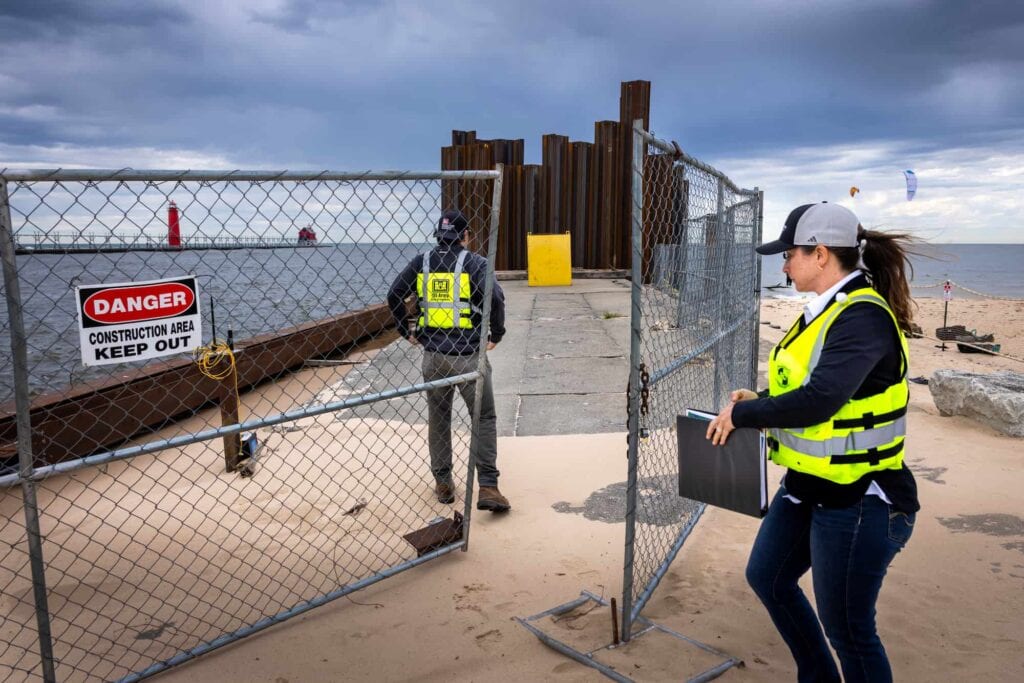Two researchers in safety vests enter a fenced construction site along the Lake Michigan shoreline.