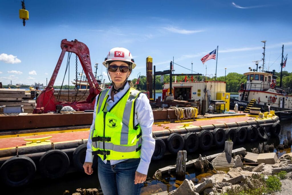 Elizabeth Wilkinson in a high-visibility vest and hard hat stands at an active waterfront construction site.