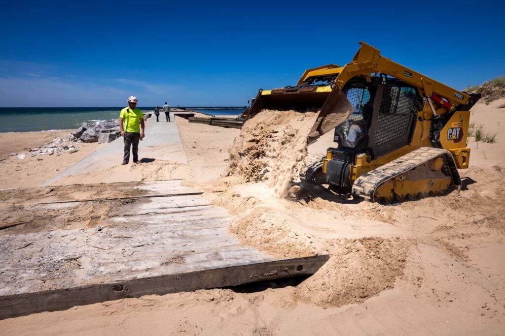 Workers use heavy machinery to move sand along a pier.