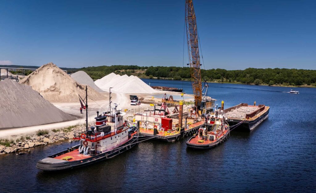 Aerial view of barges, cranes, and construction equipment, alongside a body of water.