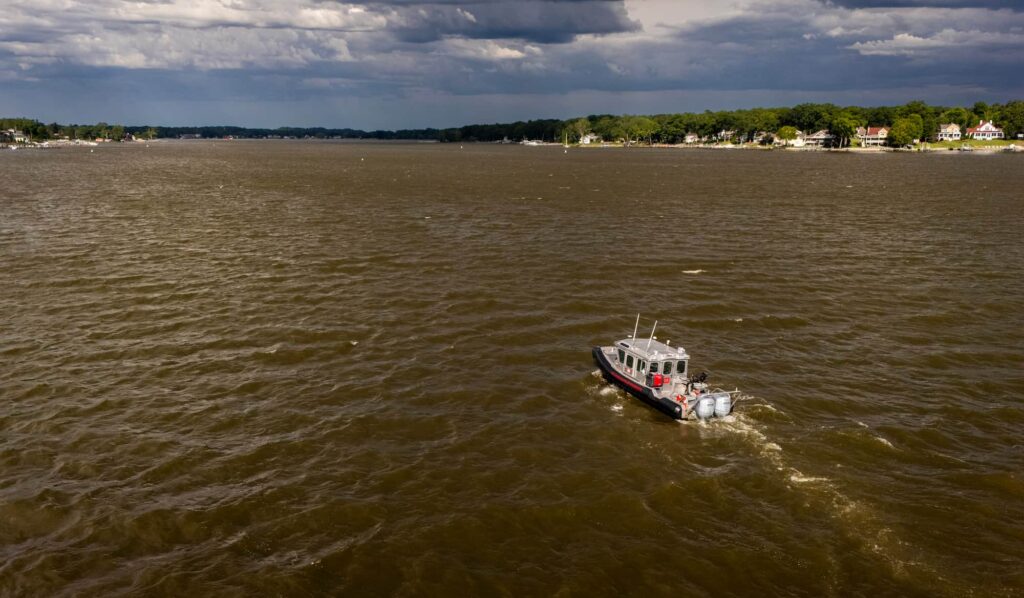 A research vessel travels across Lake Michigan beneath dark storm clouds near the shoreline.