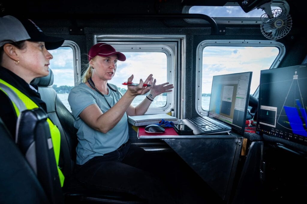Researchers inside the boat's cabin review equipment and discuss data collection during a field survey.