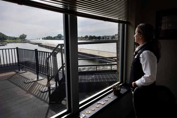 Elizabeth Wilkinson stands inside an office looking out large windows over a river and dock.
