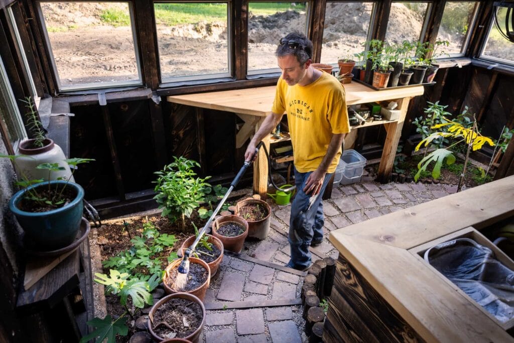 Pete Cook works in a greenhouse-like growing space filled with plants and garden beds.