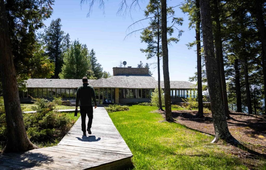 Pete Cook walks along a wooden boardwalk leading through a forested property toward a house.