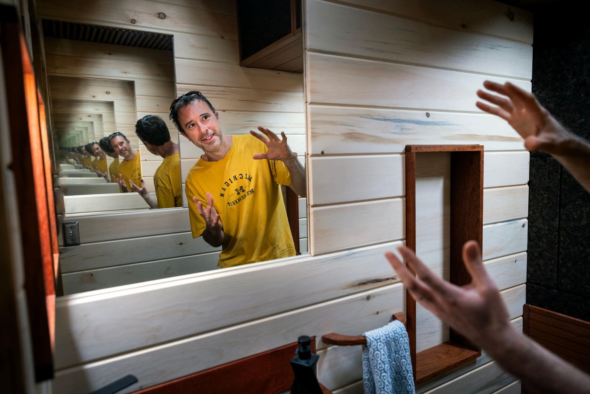 Cook gestures toward an infinitive mirror while standing inside the compact bathroom.