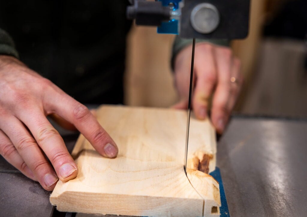 Close-up of hands cutting a piece of wood on a band saw during a woodworking project.