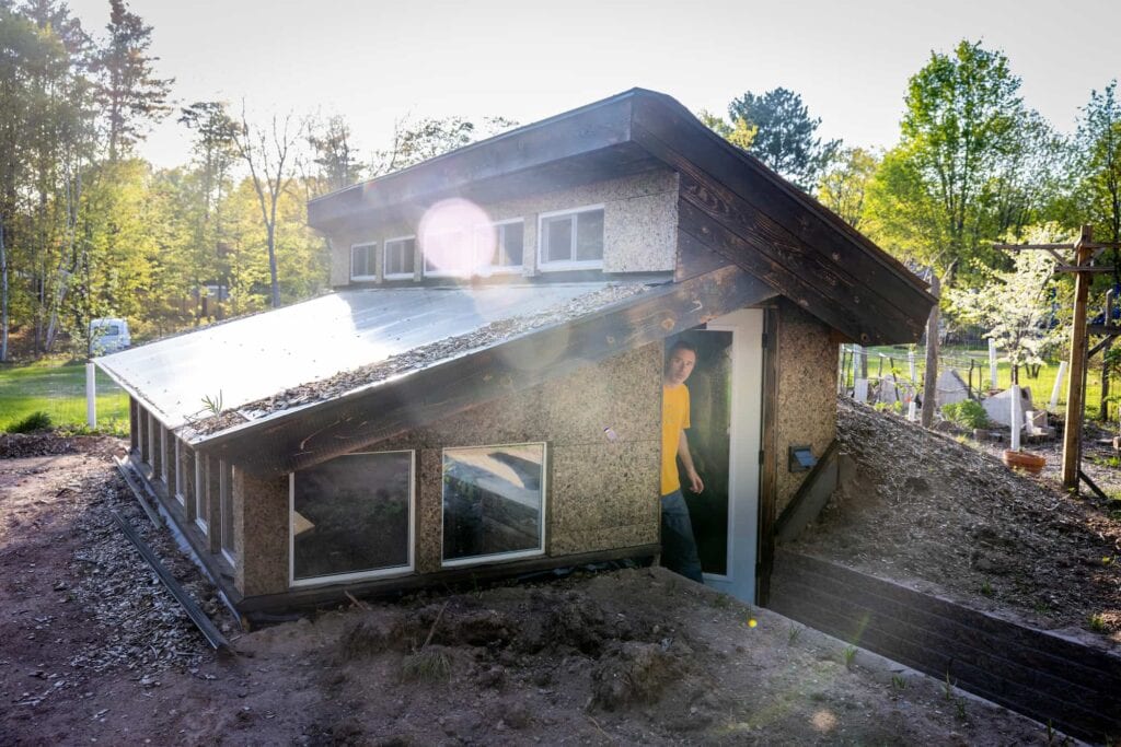 Sunlight shines on a small eco-friendly building surrounded by trees and natural vegetation.
