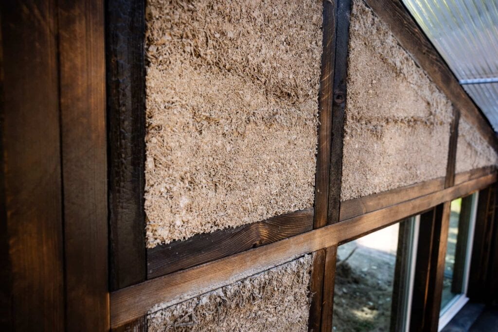 Close-up of a natural building wall showing wood framing and a textured insulation or earthen construction material.