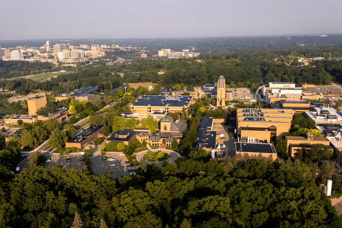An aerial photograph of the University of Michigan North Campus, surrounded by woods with Central Campus in the background.