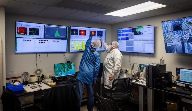 Two men point up at bright red spot in a black box on a screen.
