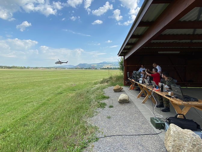 A helicopter flies low over a field while a team of researchers sit under a nearby barn with computers and other electronic equipment.