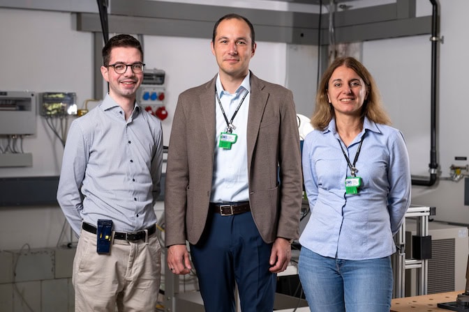 Three researchers stand side-by-side in a lab environment, smiling.