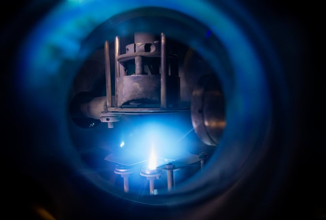 A view through a window reveals a blue flame shining into a metal clamp.